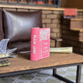 Load image into Gallery viewer, Pink book titled 'Plain Jane Vanilla' on a wooden table with a cozy retro indoor setting.
