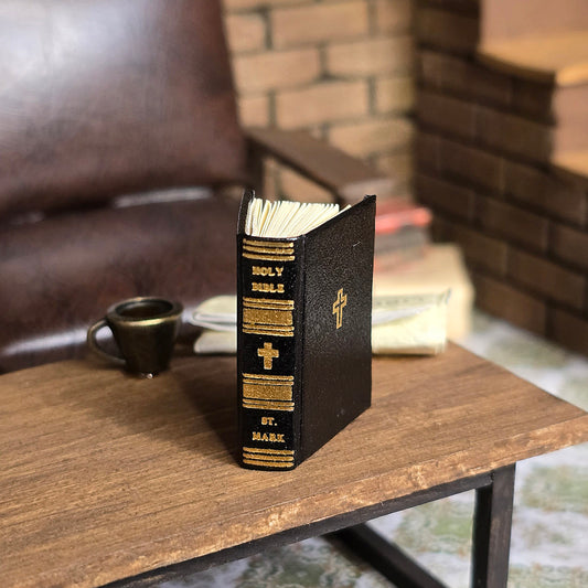 Small black leather-bound bible with gold text on a wooden surface, with a blurred background.