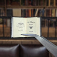 Load image into Gallery viewer, Miniature book titled 'The Gospel According to Mark' held open by tweezers with a blurred bookshelf background.
