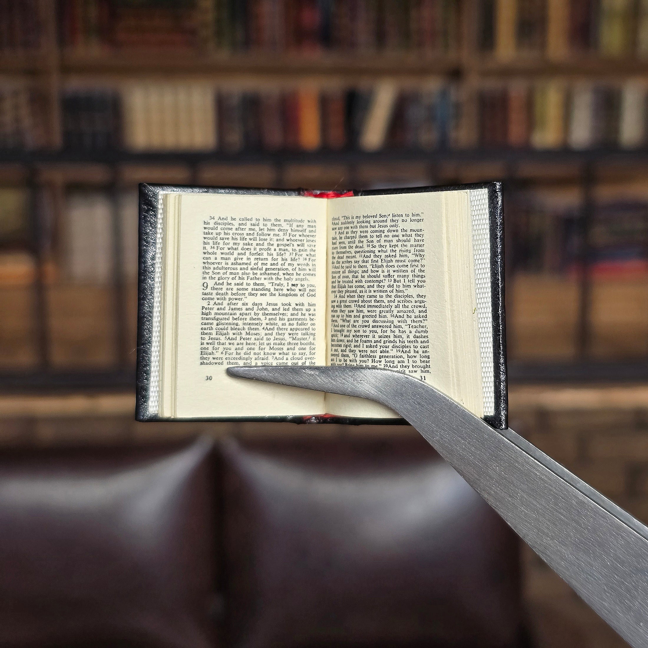 Open book held by tweezers against a blurred bookshelf background