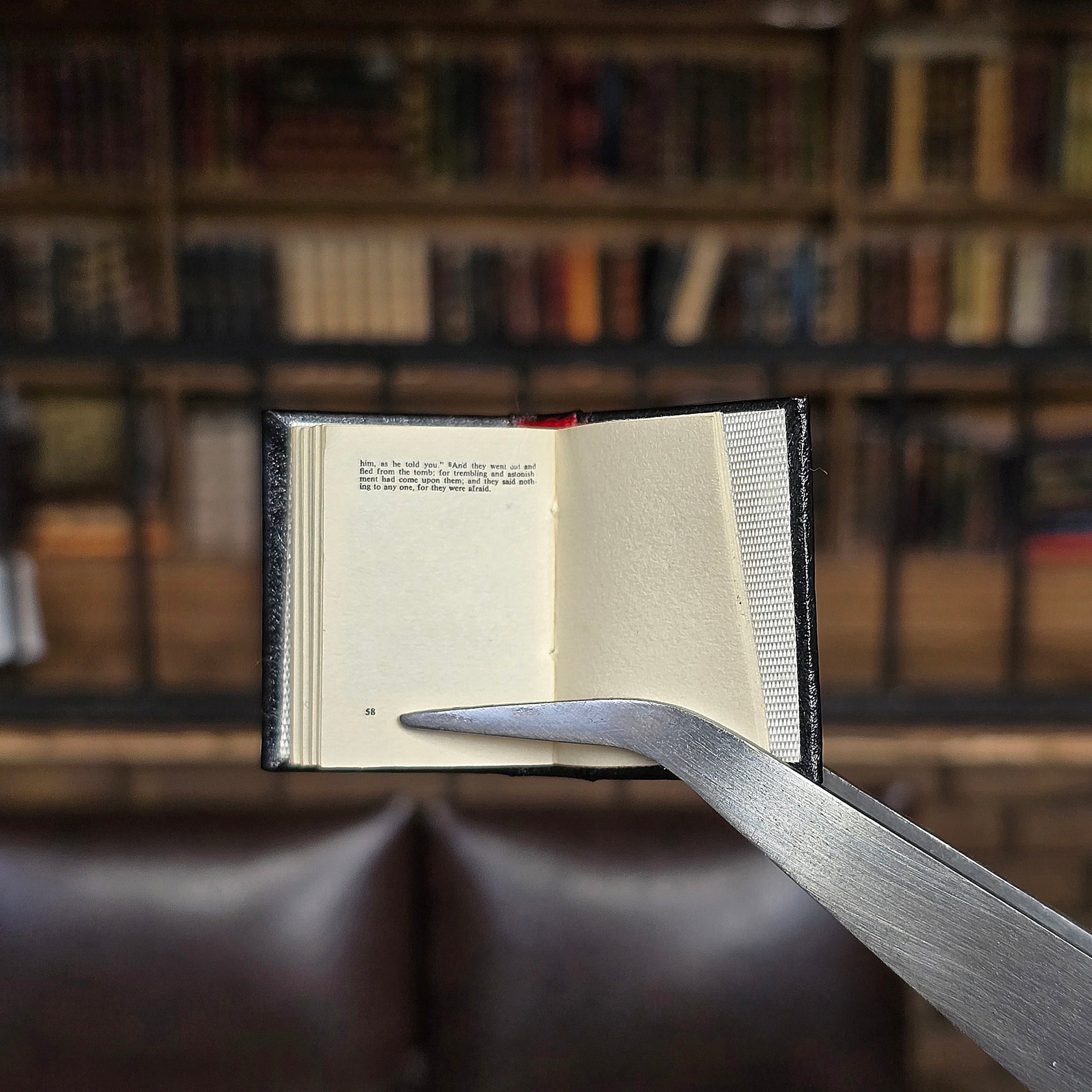 Open book held by tweezers in front of a blurred bookshelf background