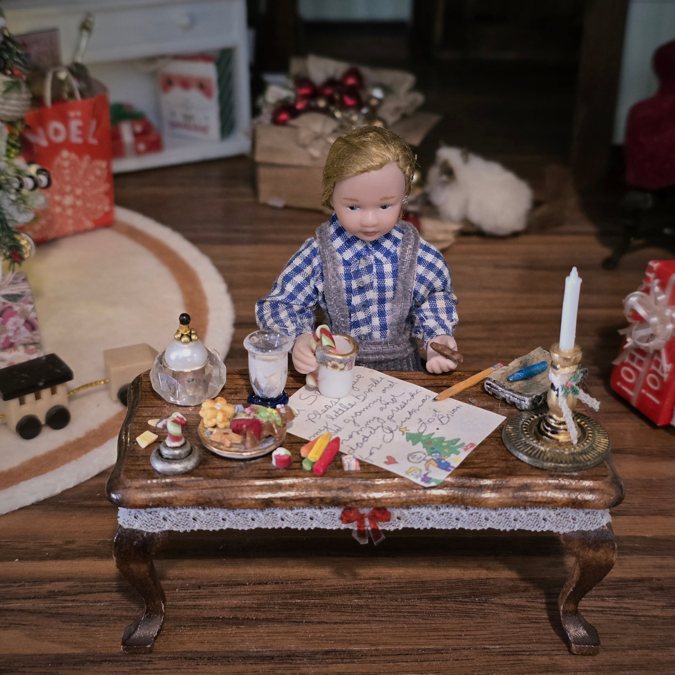 Doll in a checkered outfit sitting at a miniature table with various holiday items in a festive setting.