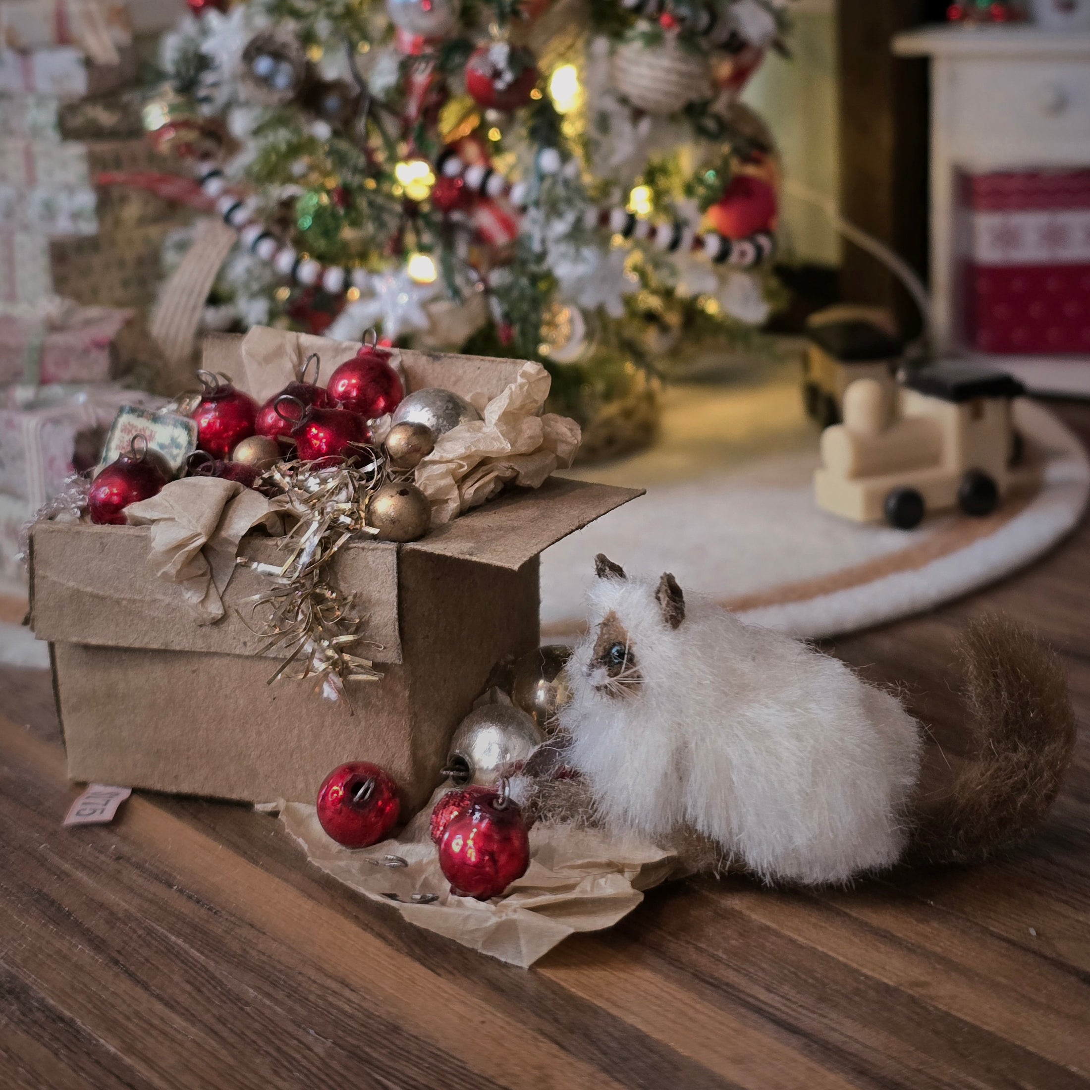 Small cat playing with Christmas decorations on a wooden floor.
