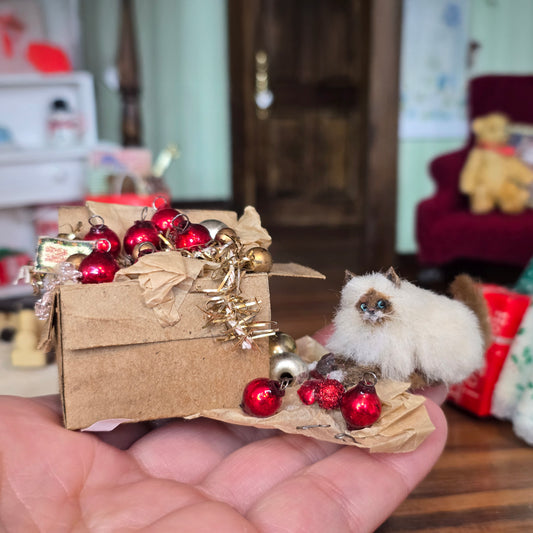 Small decorative box with red ornaments and a miniature cat on a person's palm.