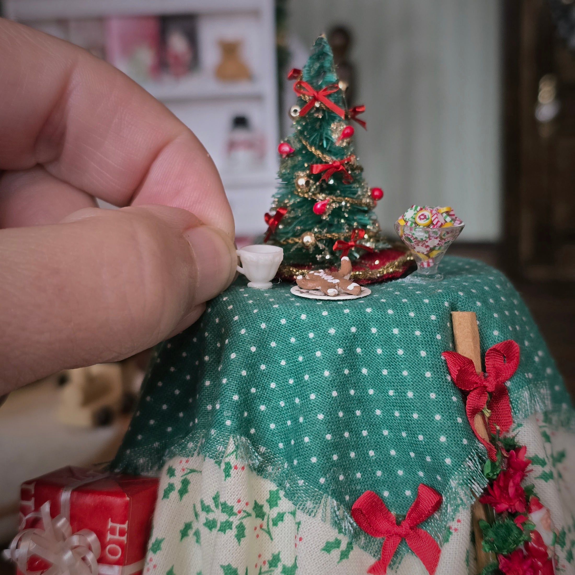 Miniature Christmas scene with a tree, presents, and decorations on a tablecloth.