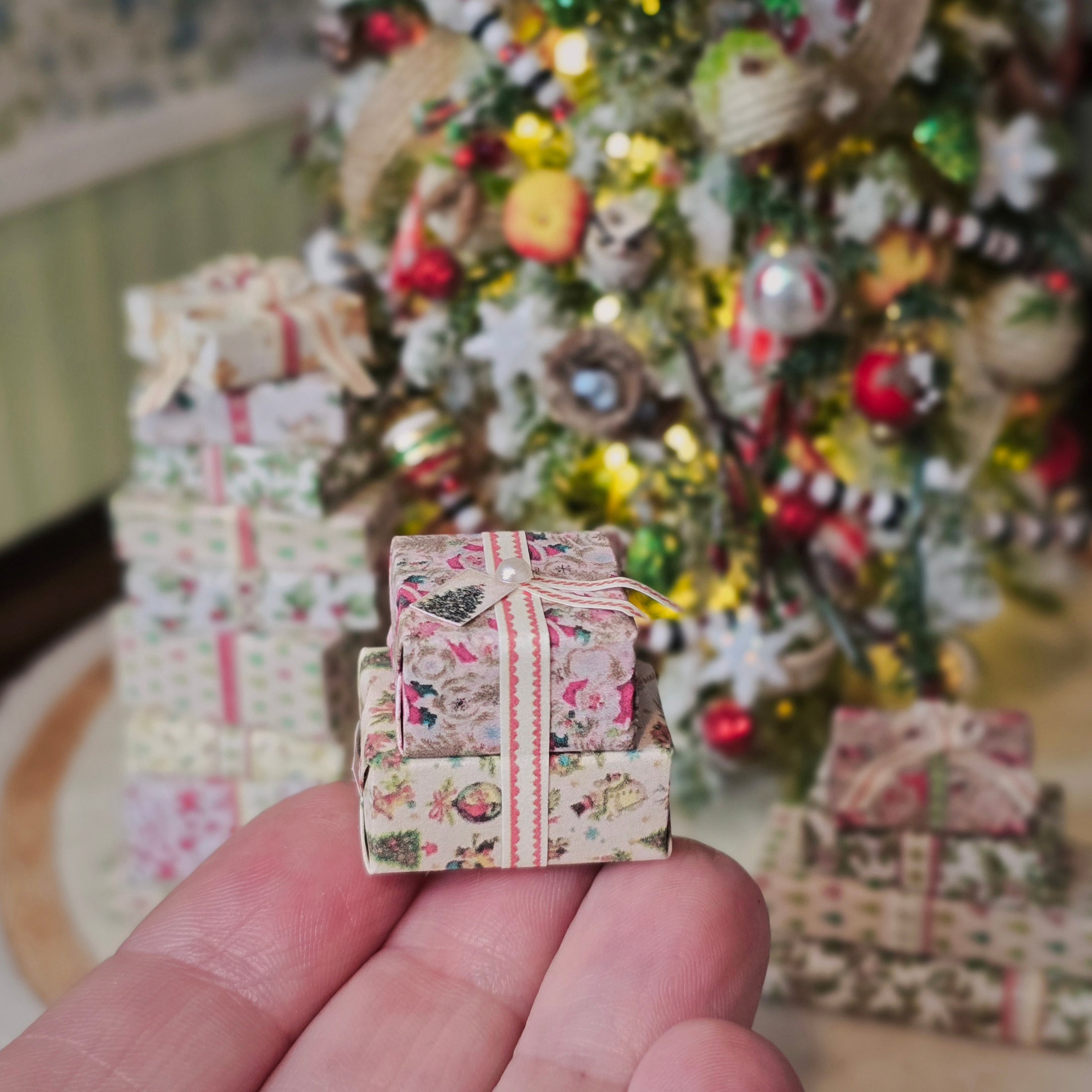 Miniature gift box held in front of a decorated Christmas tree with presents.