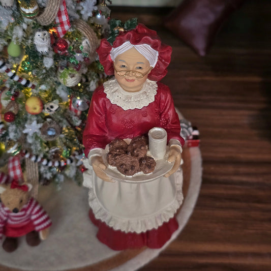 Mrs. Claus doll holding cookies in front of a Christmas tree.
