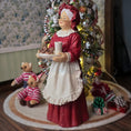 Load image into Gallery viewer, Mrs. Claus doll holding a plate of cookies in front of a Christmas tree.
