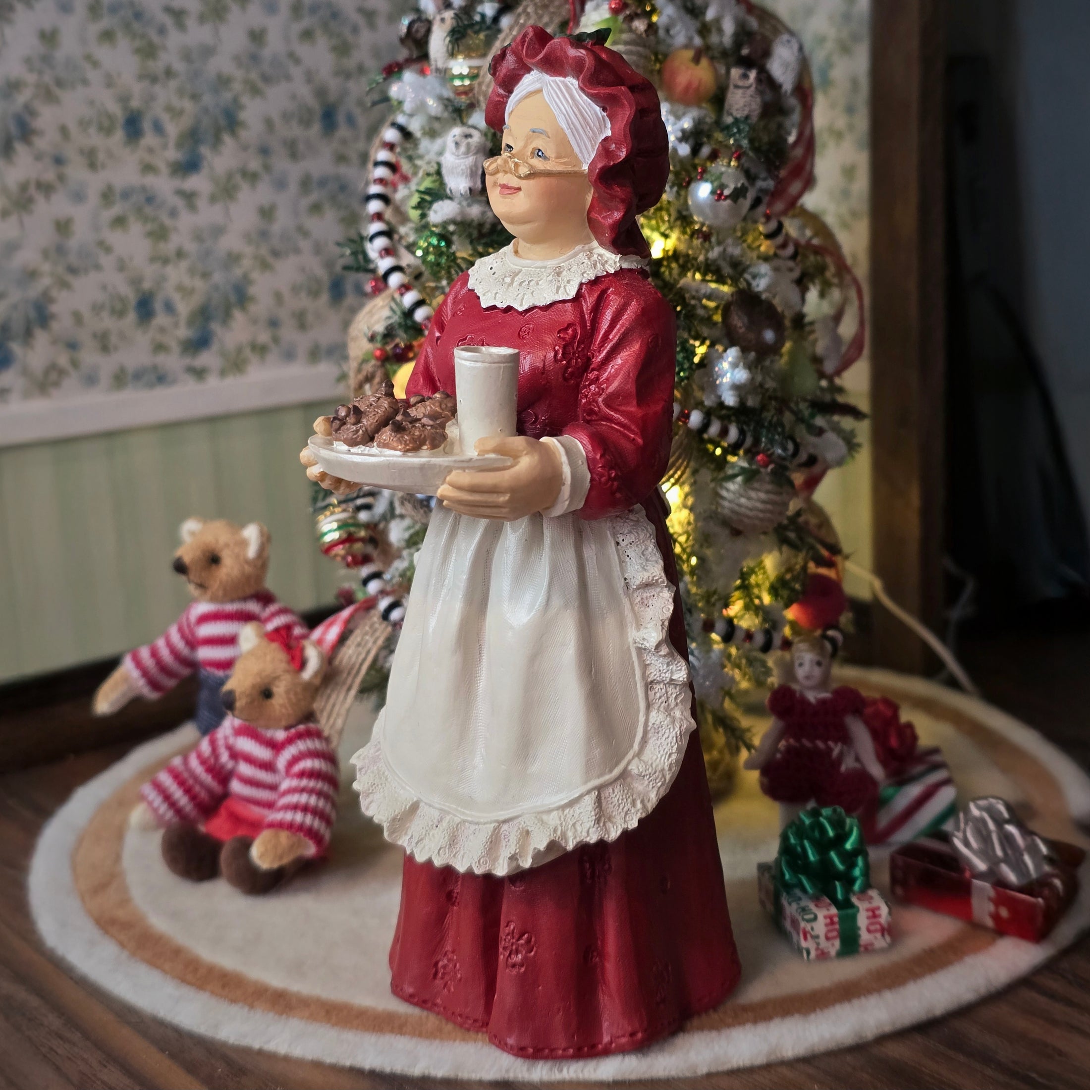 Mrs. Claus doll holding a plate of cookies in front of a Christmas tree.