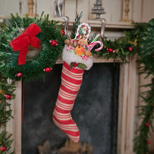 Decorative Christmas stocking with candy and wreath hanging on a fireplace mantel.