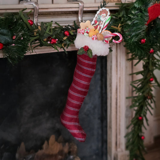 Red striped Christmas stocking with candy canes and and toys hanging on a fireplace mantel.