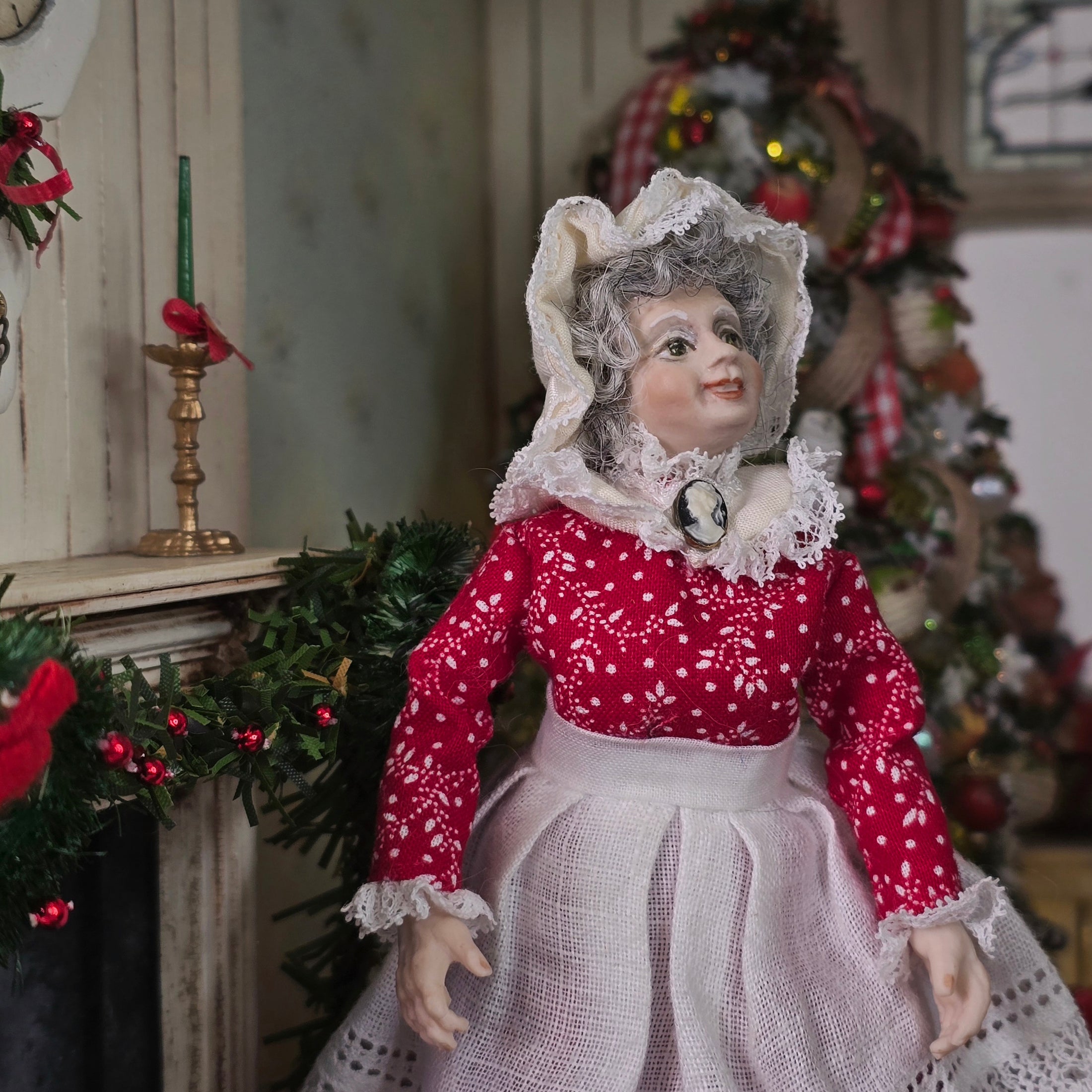 Mrs. Claus miniature doll in a red dress with white lace details, standing in a decorated room.