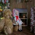 Load image into Gallery viewer, Teddy bear and  Christmas girl doll by artisan Carol McBride in a cozy room with a Christmas tree and wooden furniture.
