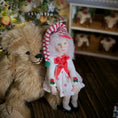 Load image into Gallery viewer, Teddy bear and  Christmas girl doll by artisan Carol McBride with festive hat and dress in a decorated room

