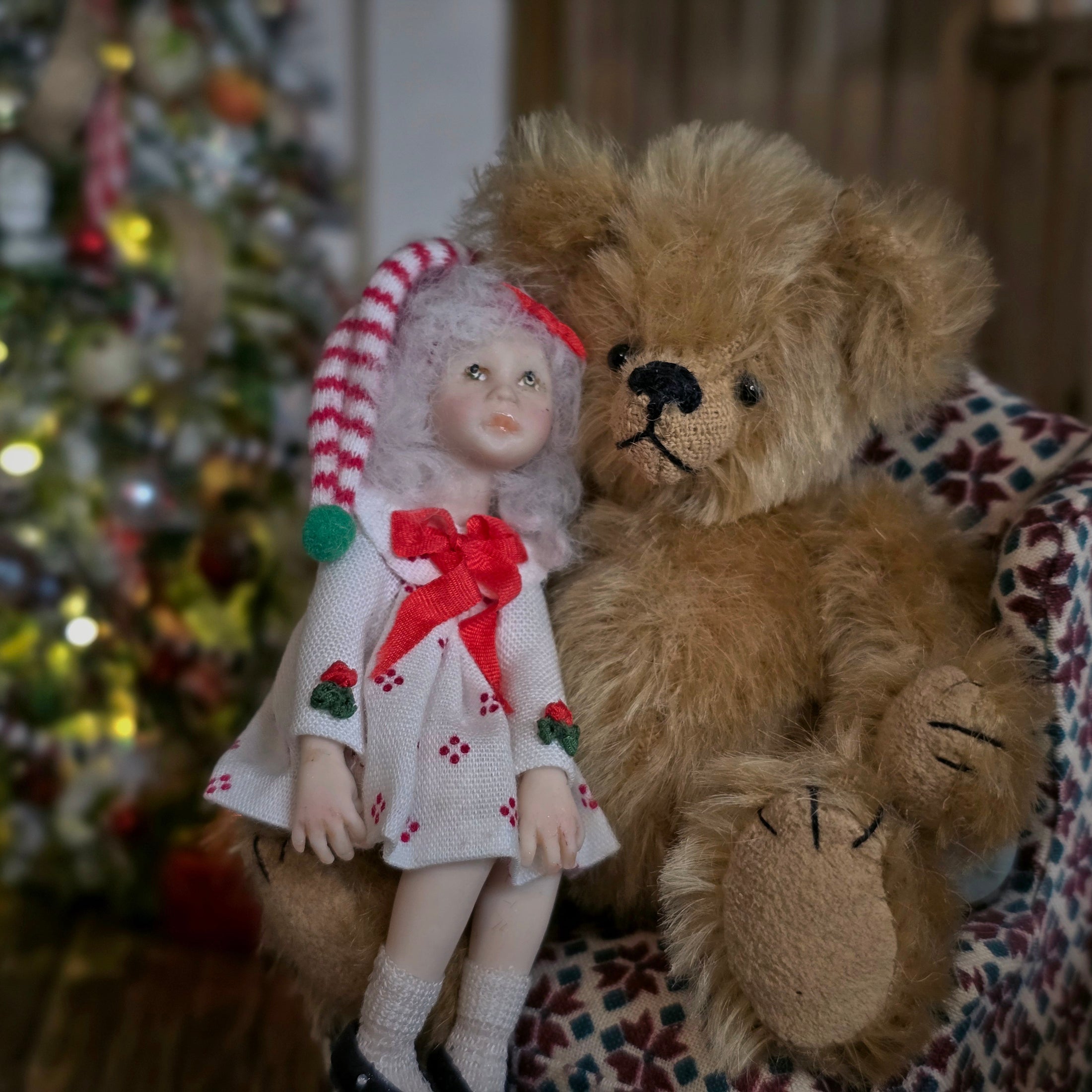 Vintage-style teddy bear and  Christmas girl doll by artisan Carol McBride with a Christmas tree in the background