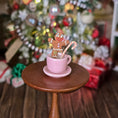 Load image into Gallery viewer, Pink mug with gingerbread man and candy cane on a wooden stand, Christmas tree and presents in the background
