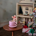 Load image into Gallery viewer, Pink mug with a gingerbread man and candy cane on a small table, blurred Christmas scene in the background.
