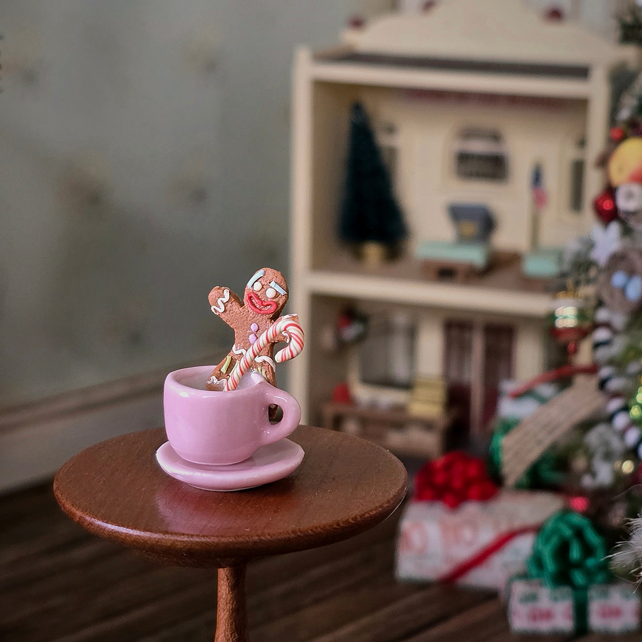 Pink mug with a gingerbread man and candy cane on a small table, blurred Christmas scene in the background.