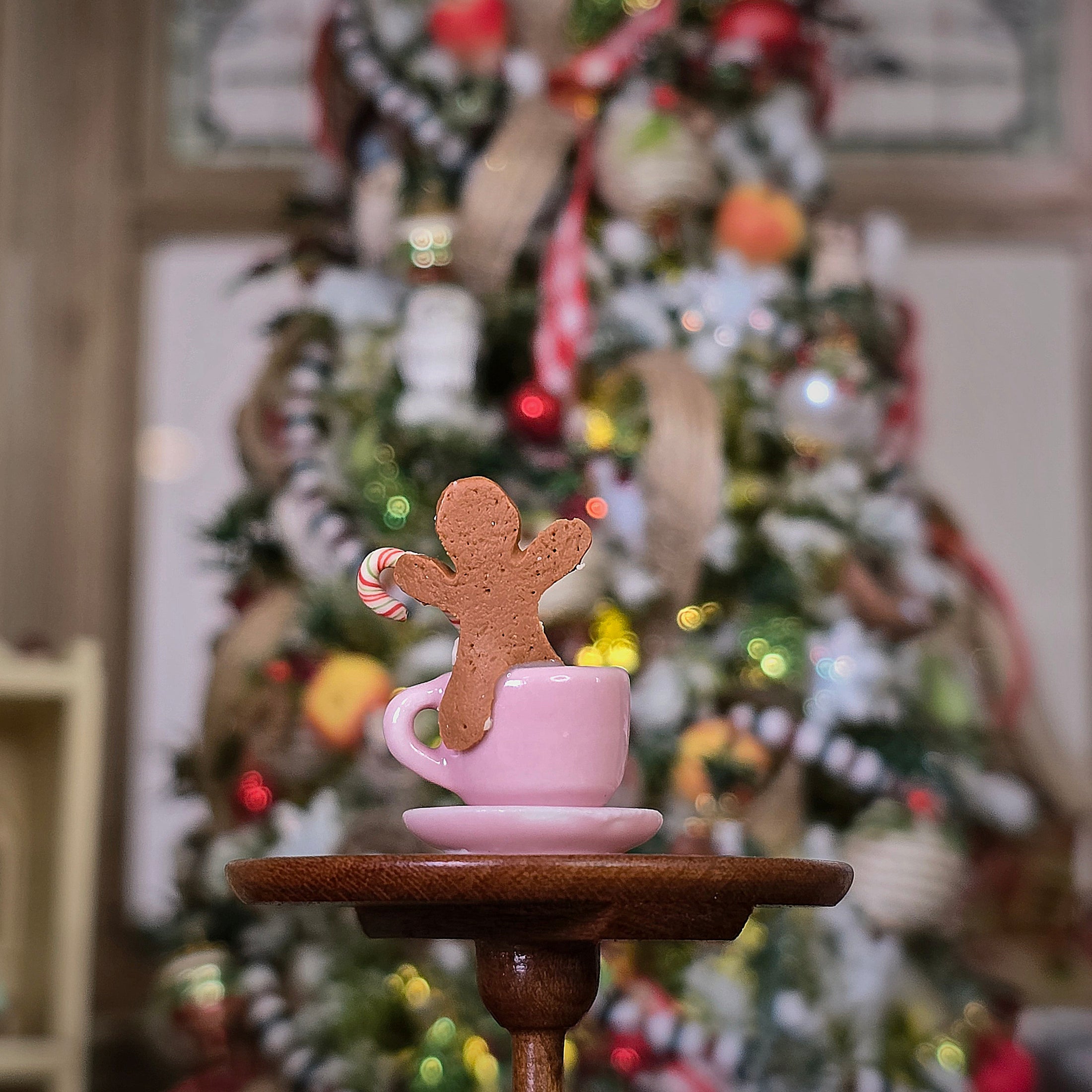 Gingerbread man cookie on a pink cup with a Christmas tree in the background