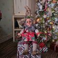 Load image into Gallery viewer, Decorative elf doll holding a gift in front of a Christmas tree.
