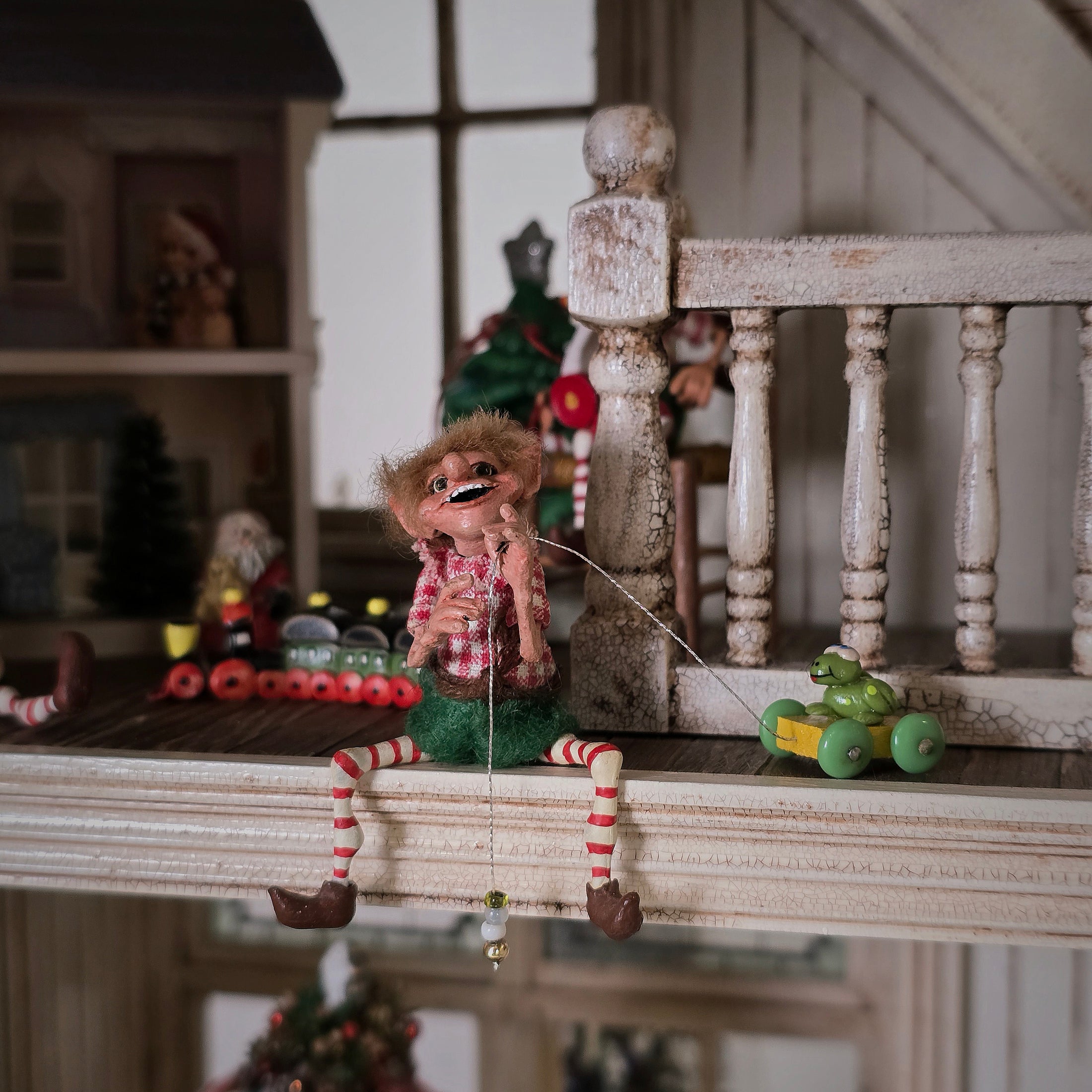 Miniature Grinning Elf Christmas Doll Cynthia Baron sitting in a wooden loft.