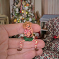 Load image into Gallery viewer, Grinning Elf Christmas Doll Cynthia Baron held in a hand with a decorated Christmas tree in the background
