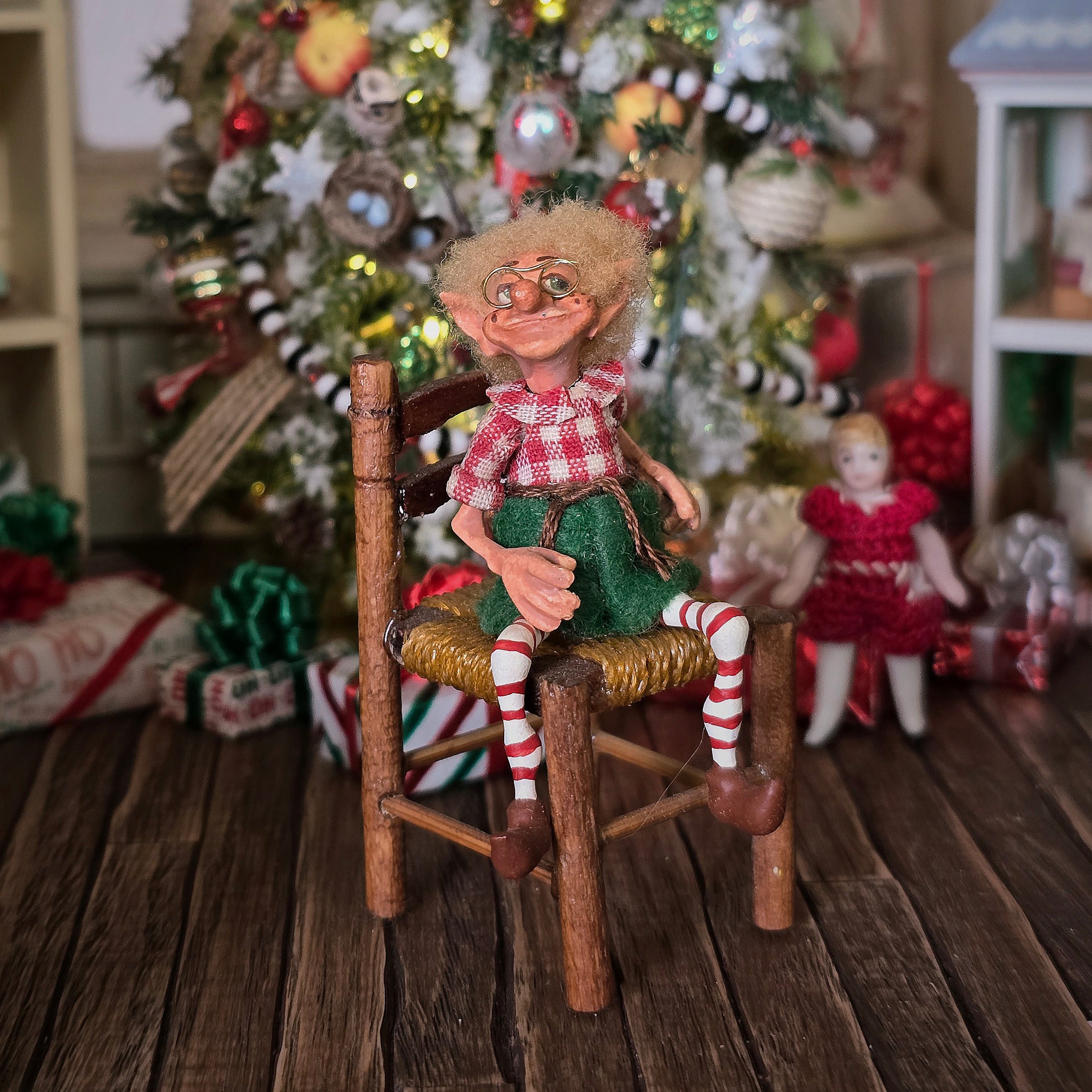 Christmas elf with glasses by artist Cynthia Baron, in chair