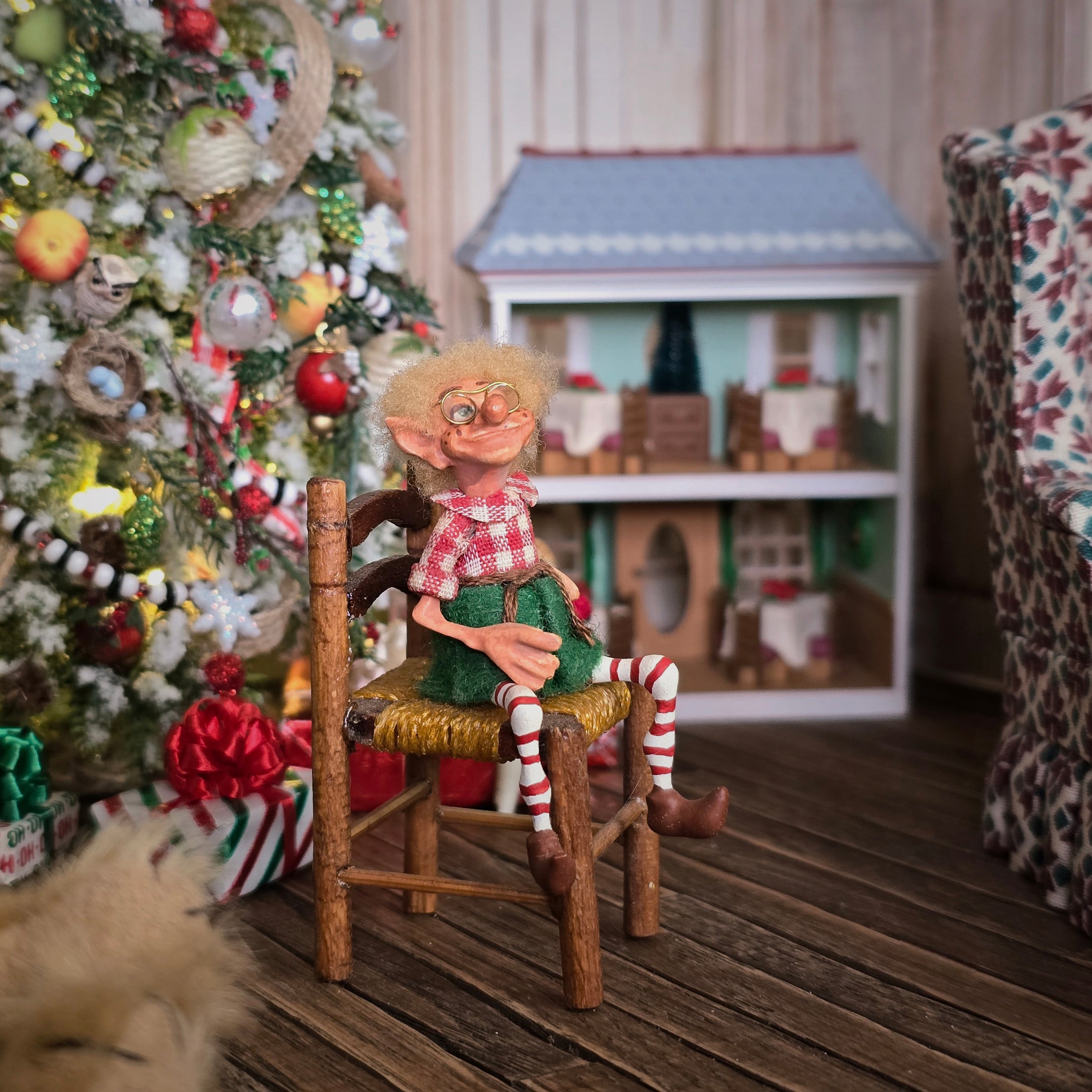 Christmas elf with glasses by artist Cynthia Baron, in chair