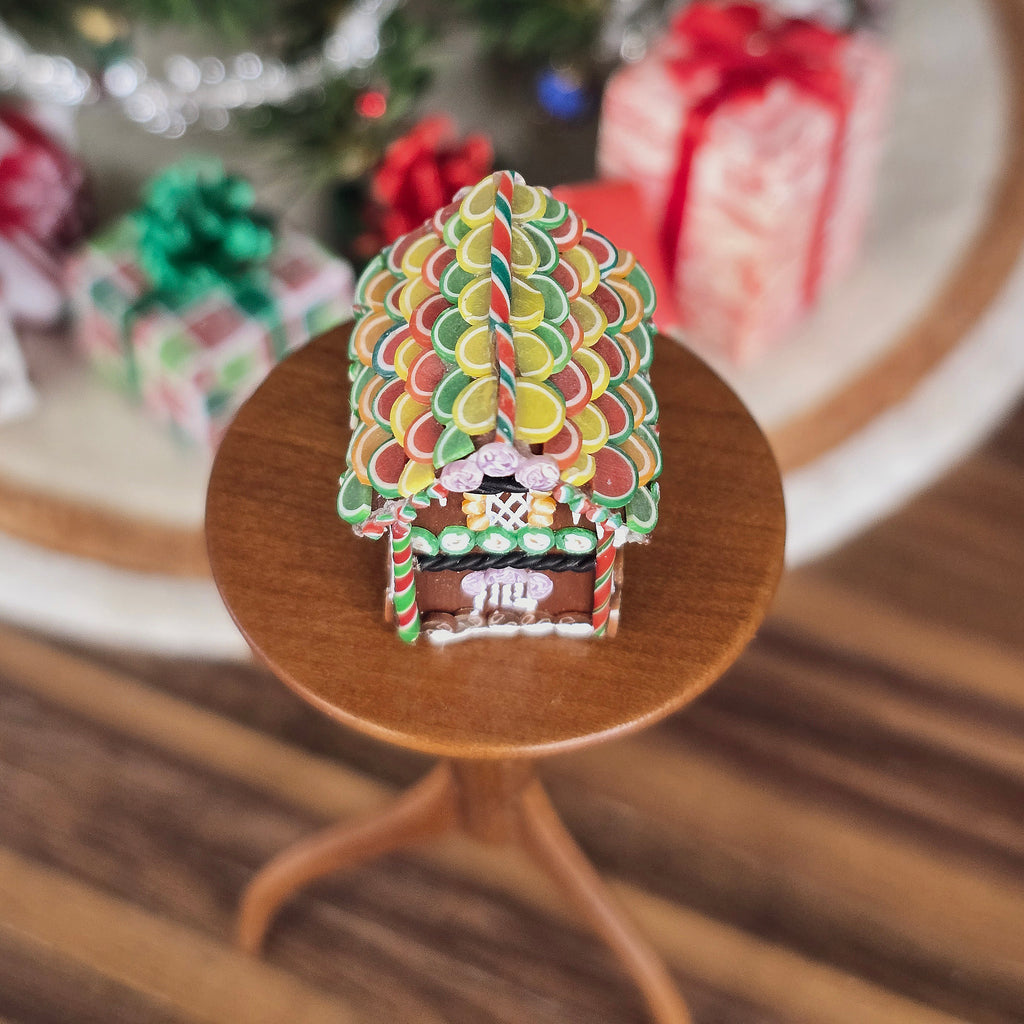 Colorful gingerbread house on a small wooden stand with Christmas decorations in the background.