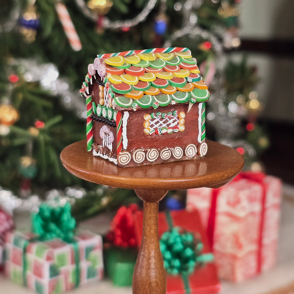 Gingerbread house on a small wooden stand with Christmas decorations in the background