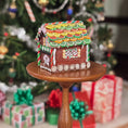 Load image into Gallery viewer, Gingerbread house on a small wooden stand with Christmas decorations in the background
