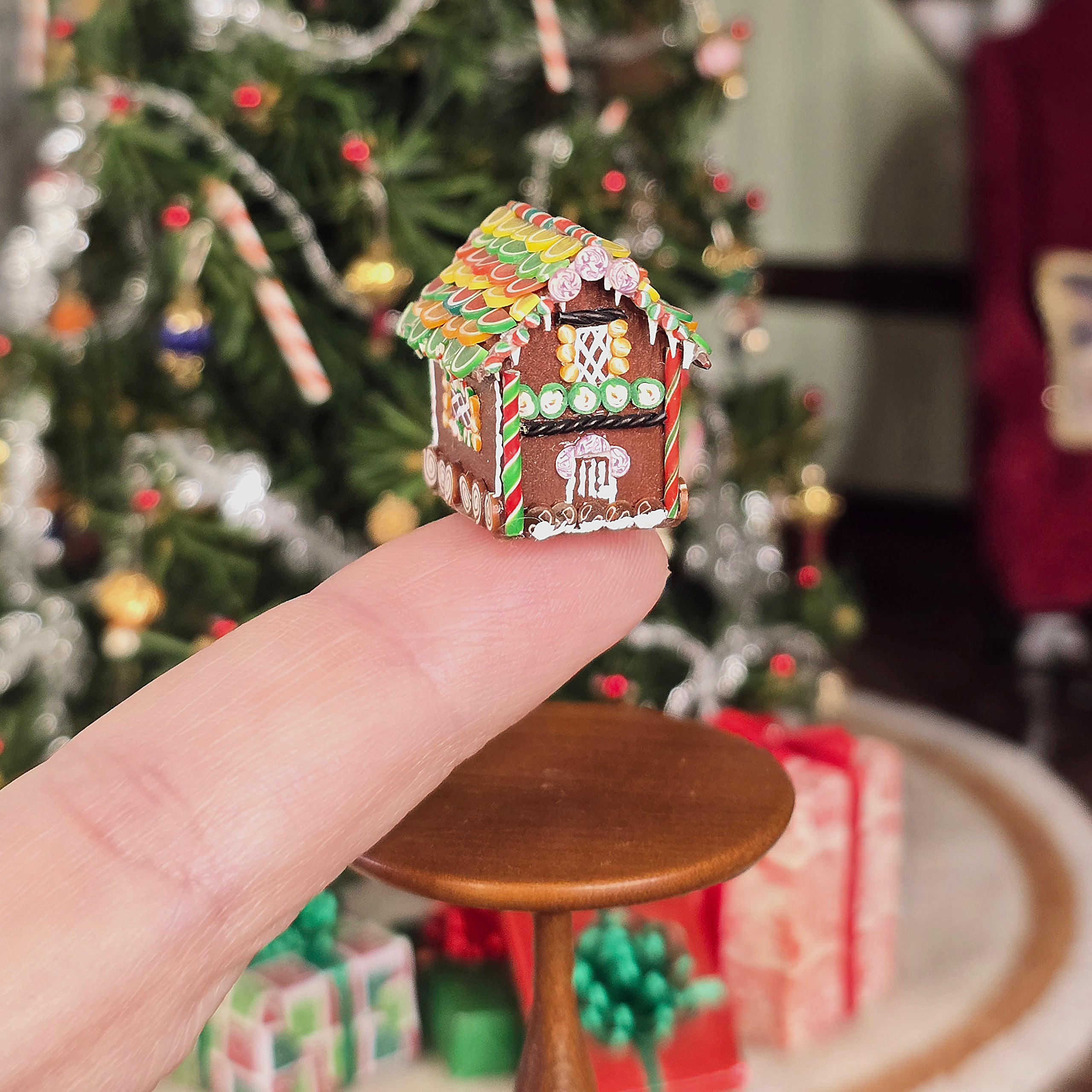 Miniature gingerbread house held in front of a decorated Christmas tree.