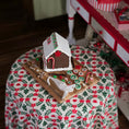 Load image into Gallery viewer, Gingerbread house on a wooden board with candy canes on a floral tablecloth.
