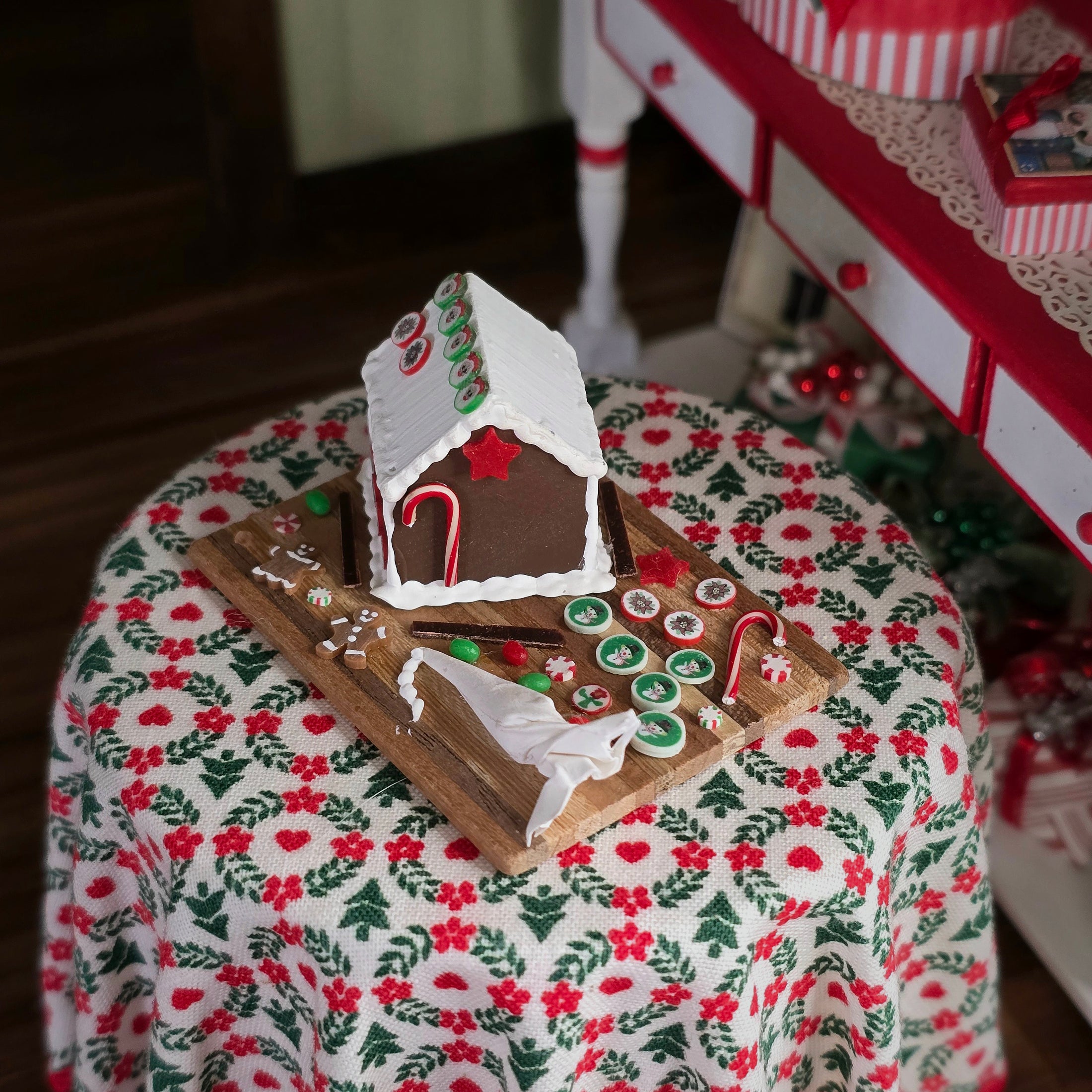 Gingerbread house on a wooden board with candy canes on a floral tablecloth.