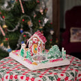 Load image into Gallery viewer, Decorative gingerbread house with candy decorations on a table in front of a Christmas tree.
