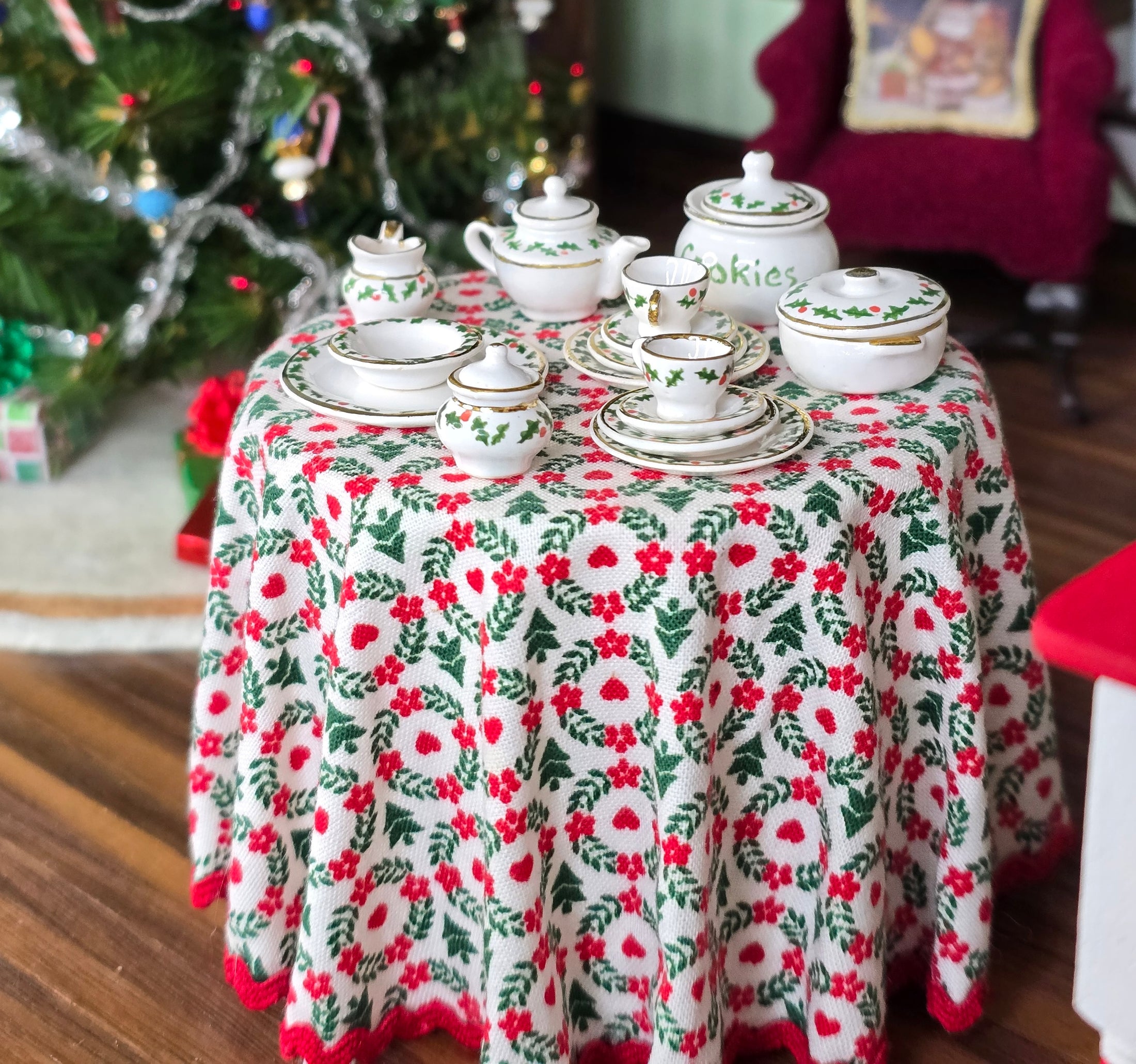 Miniature Christmas tea set on a table with a floral tablecloth in a festive setting.