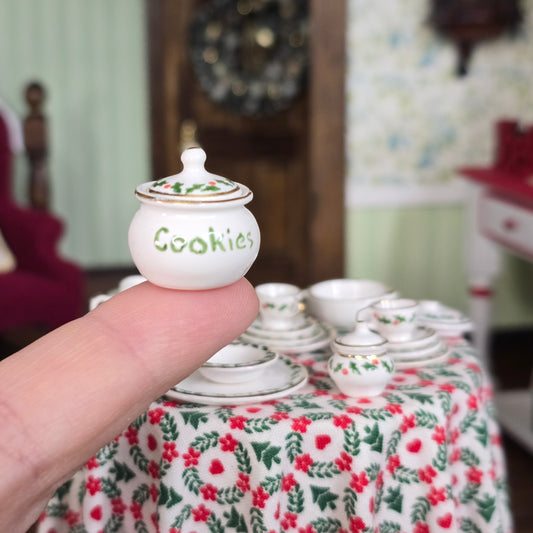 Small white cookie jar labeled 'Cookies' held by a finger
