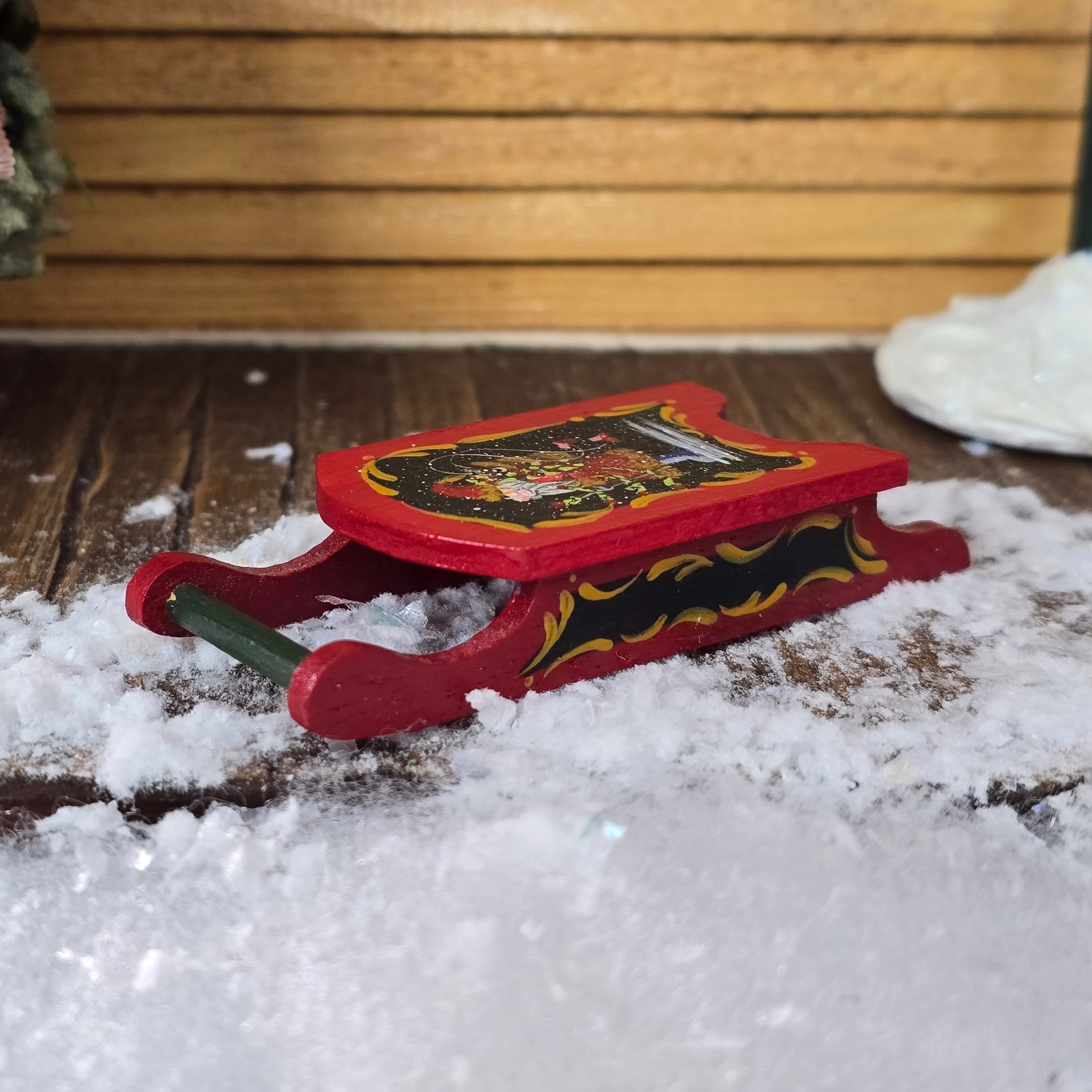 Red toy sleigh with a Christmas design on a snowy surface 