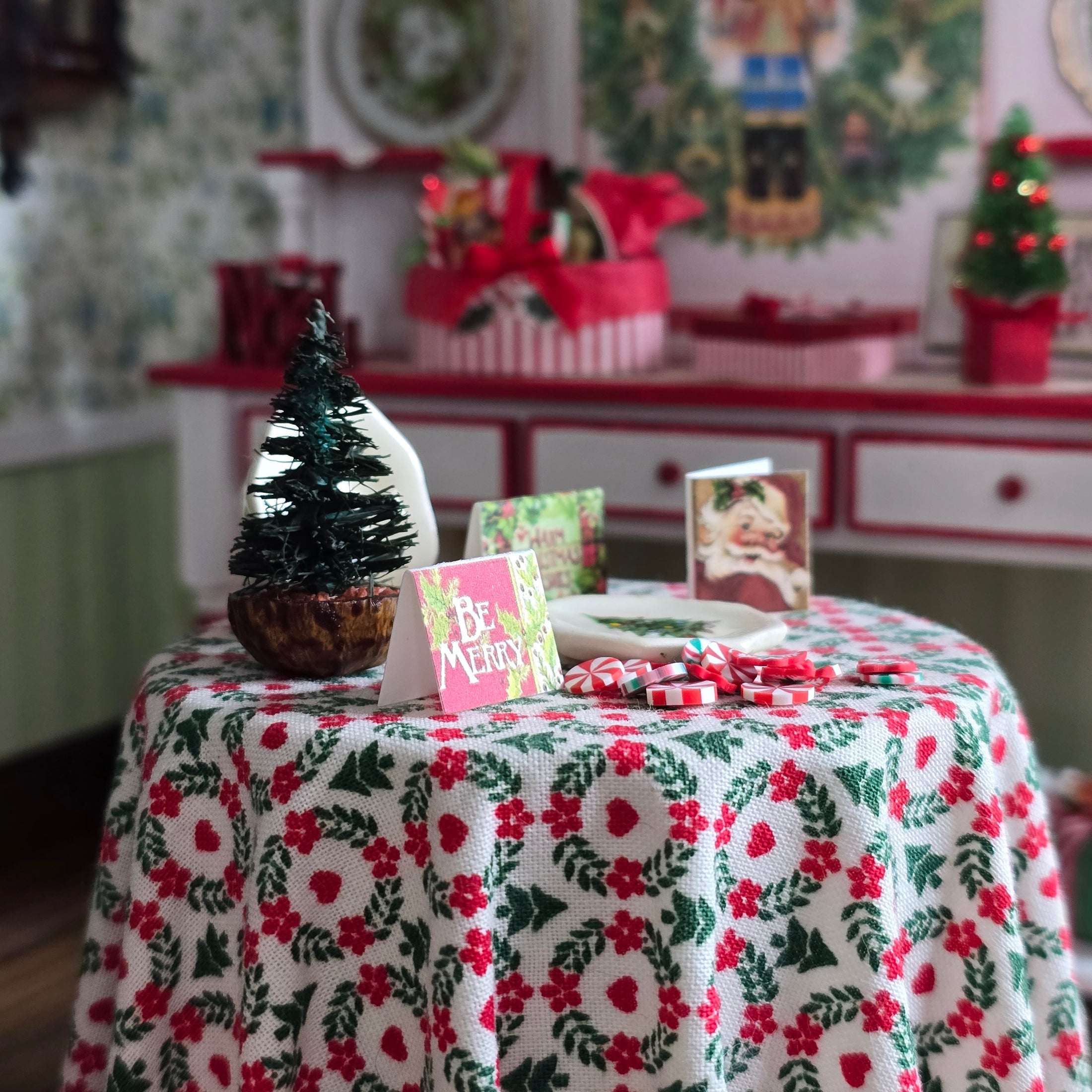 Decorative table setting with a floral tablecloth, small Christmas tree, and cards in a festive room.