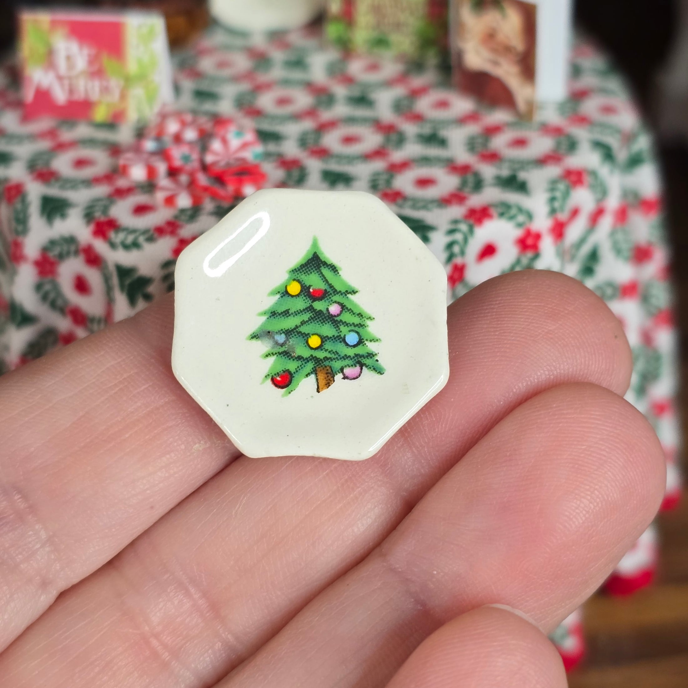 Small hexagonal object with a Christmas tree design held in a hand, with a festive tablecloth in the background.