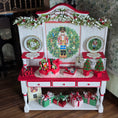 Load image into Gallery viewer, Decorative Christmas cabinet with wreaths, nutcrackers, and gift boxes on a wooden floor.
