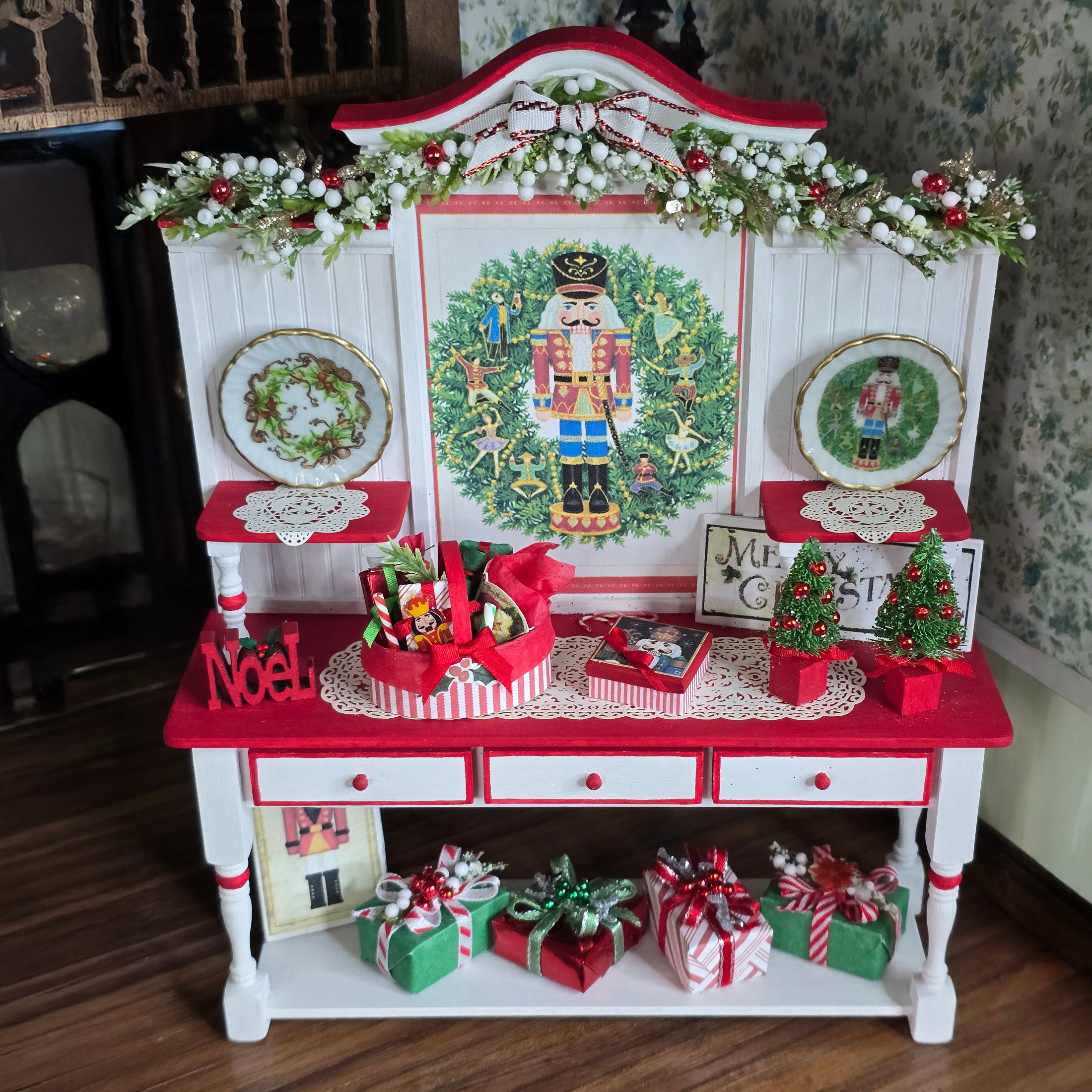 Decorative Christmas cabinet with wreaths, nutcrackers, and gift boxes on a wooden floor.
