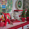 Load image into Gallery viewer, Christmas-themed decor with trees, gift boxes, and a 'Merry Christmas' sign on a red surface.
