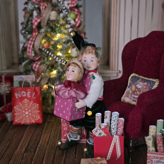 Elf boy doll carrying jack-in-the-box toy in front of a decorated Christmas tree with presents underneath.