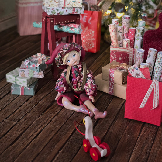 Hand-Sculpted Clay Elf Boy in Raspberry Pink with floral outfit surrounded by wrapped gifts on a wooden floor