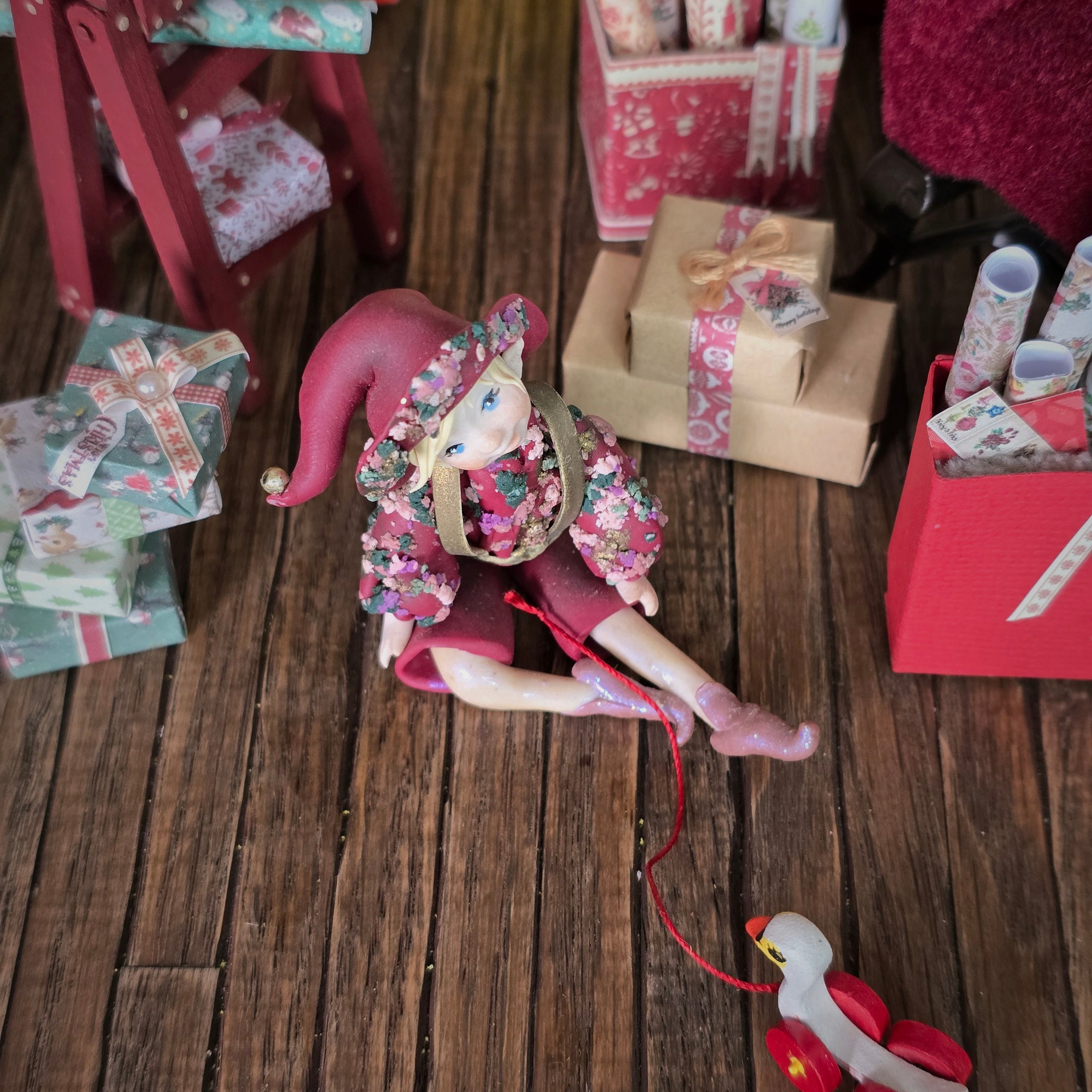 Hand-Sculpted Clay Elf Boy in Raspberry Pink with floral details on a wooden surface with gift boxes.