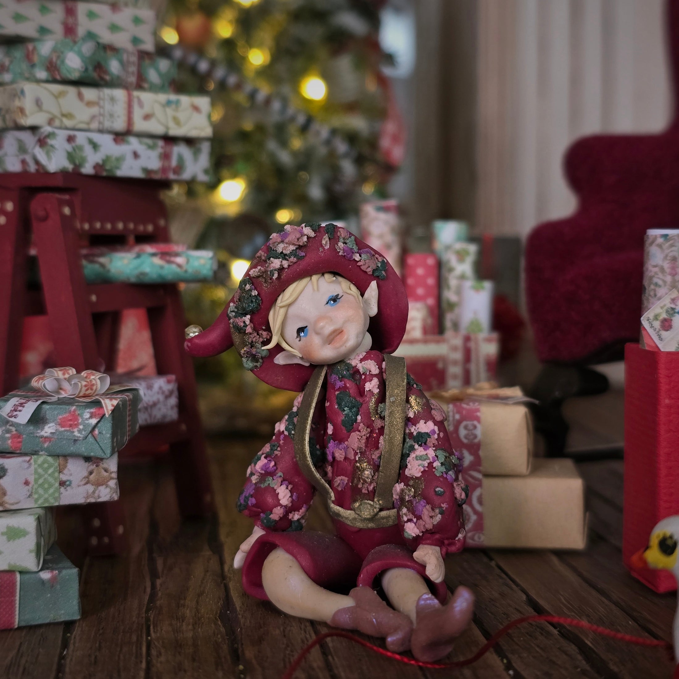 Hand-Sculpted Clay Elf Boy in Raspberry Pink in a festive setting with Christmas tree and presents.