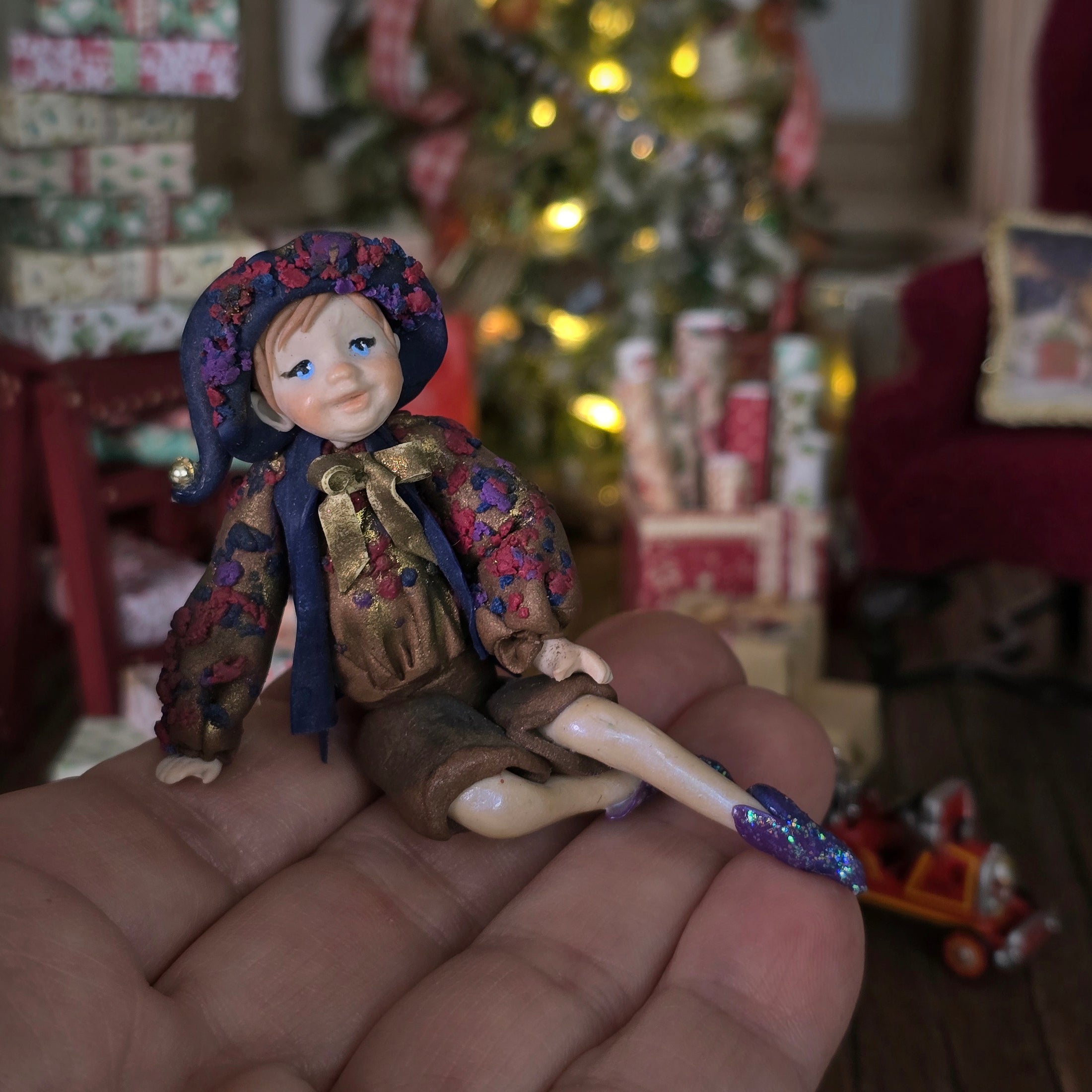 Sculpted clay elf boy doll wearing a purple outfit sitting on a hand