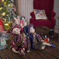 Load image into Gallery viewer, Two elf boy dolls in floral outfits sitting on a wooden floor with a decorated Christmas tree and red chair in the background.
