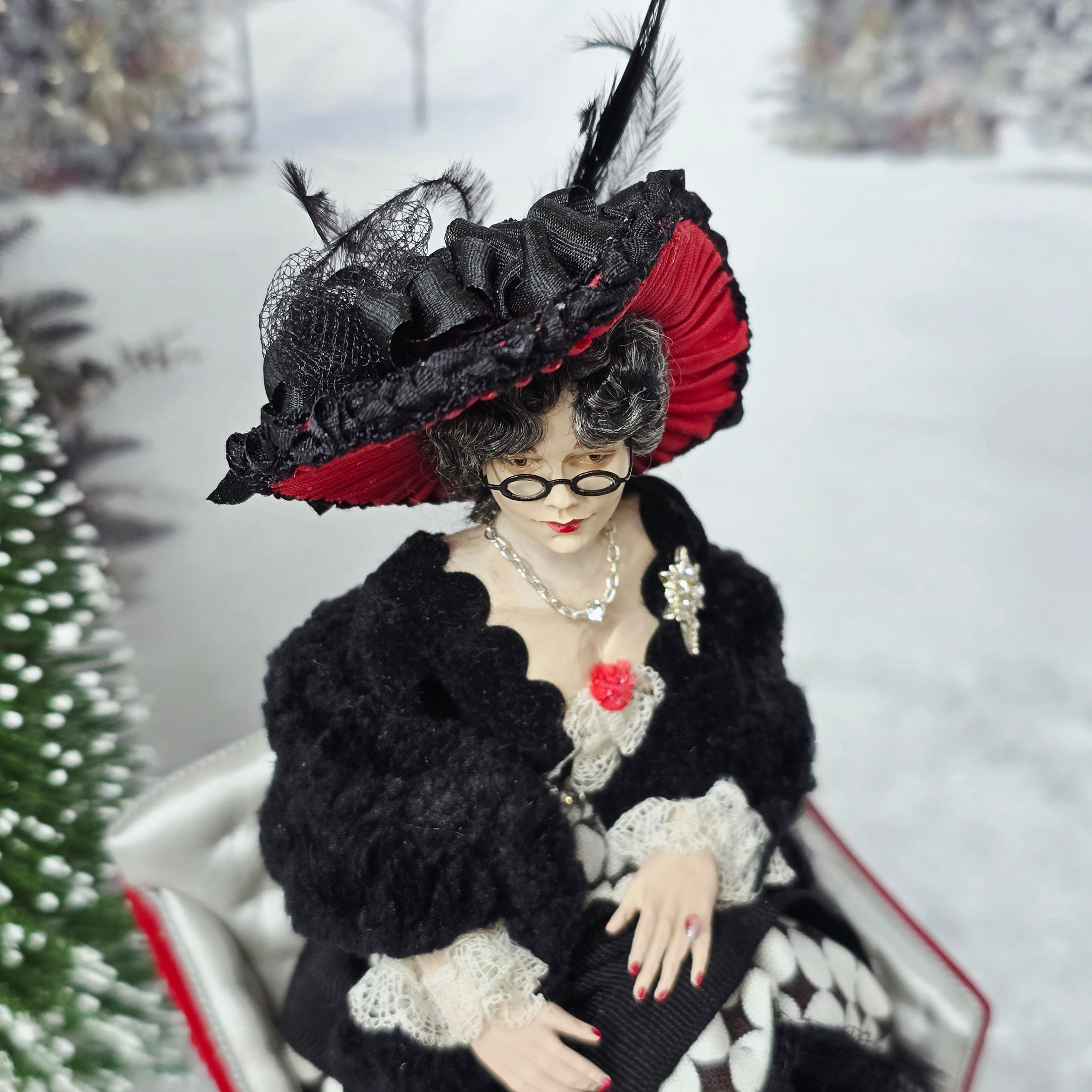 “Winter Lady” Doll in a black and red hat with feathers, sitting in a sleigh with a snowy background.